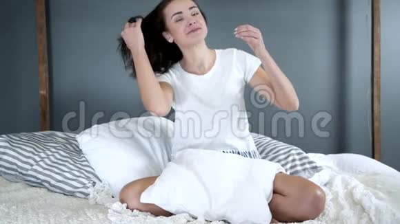 一个微笑的女人躺在床上早晨她慢悠悠地摇着头发看着镜头视频的预览图