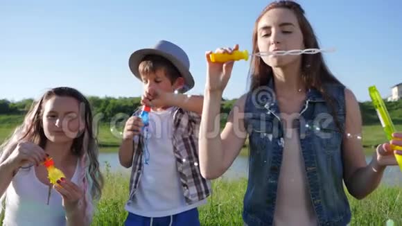 快乐的童年微笑的姐妹和弟弟在洛奇附近的草坪上做肥皂泡视频的预览图