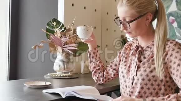 一个戴眼镜的年轻学生正在咖啡馆里学英语可爱的金发碧眼透过杂志喝茶视频的预览图
