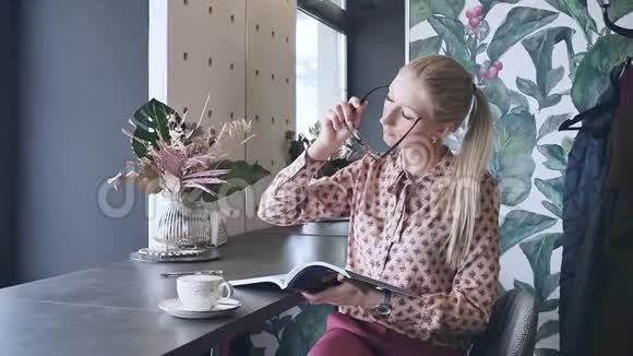 一个戴眼镜的年轻学生正在咖啡馆里学英语可爱的金发碧眼透过杂志喝茶视频的预览图