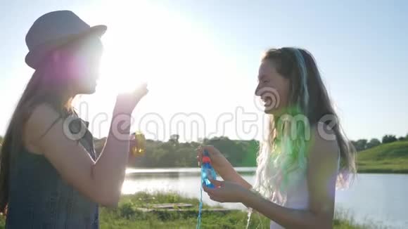 有趣的青少年带着肥皂泡的快乐姐妹在背光的草坪上快乐地度过闲暇时光视频的预览图