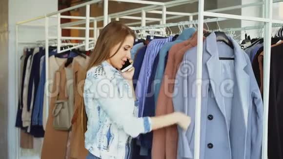 漂亮的年轻女人正在手机上聊天在豪华的精品店里买衣服她在看外套视频的预览图