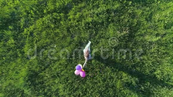 快乐女孩的空中景色看着镜头手拿着彩色气球在草地上旋转视频的预览图