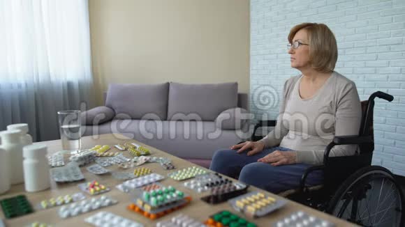 沮丧的老妇人坐在轮椅上坐在桌边吃药孤独视频的预览图