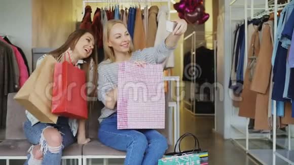 年轻女性坐在服装店里拿着五颜六色的纸袋用智能手机自拍首先是视频的预览图