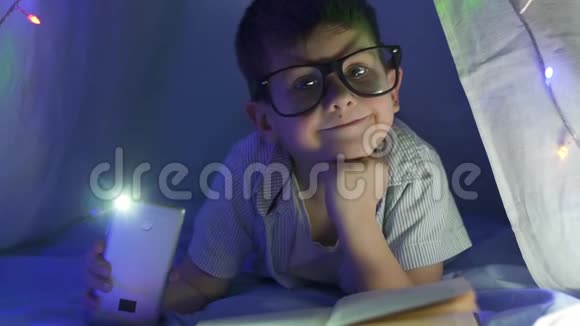 阅读书籍时手拿眼镜和手电筒的聪明孩子画像视频的预览图
