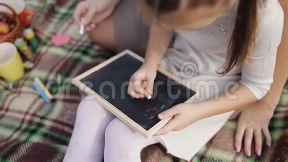 一个小女孩学会用粉笔在黑板上写字妈妈教女儿写字母字母表视频的预览图
