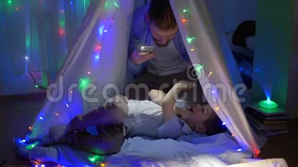 痒痒的爸爸和幼儿一起在孩子们的房间里玩得很开心晚上在假期里有生动的灯光视频的预览图