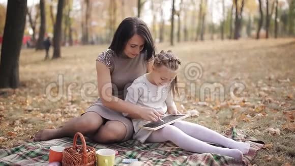 年轻漂亮的妈妈和女儿在秋天公园的粉笔板上用粉笔写字视频的预览图
