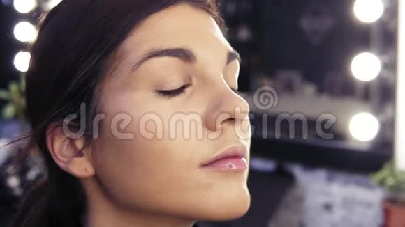 化妆师在一家美容美发店里一个漂亮的黑发女孩的脸上涂了一层粉底视频的预览图