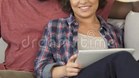 男朋友和女朋友坐在家里的沙发上在平板电脑上上网购物视频的预览图