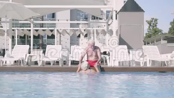 快乐的成熟夫妇一起在酒店综合体的游泳池放松坐在游泳池边上的可爱的老人视频的预览图