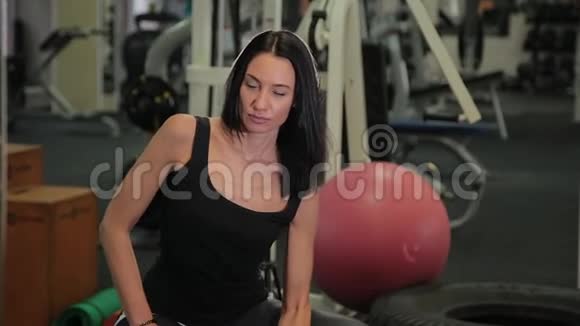 年轻的运动女性坐在健身球上在健身房训练二头肌时举起哑铃视频的预览图