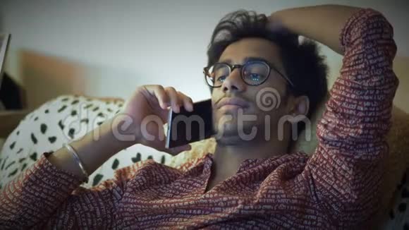 特写镜头戴眼镜的英俊印度男人在电话上坐在沙发上带着他的头发视频的预览图