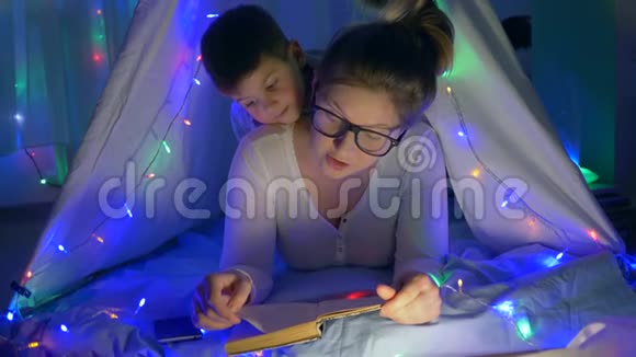 家庭氛围有爱心的妈妈读童话给孩子躺在小床上房间里放着花环视频的预览图