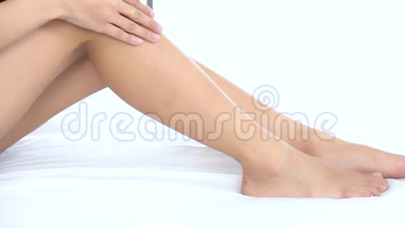 在卧室里一位美丽的年轻亚洲女人在床上摸着柔软的腿和保湿霜视频的预览图
