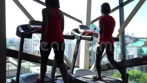 漂亮的白种人女孩在运动健身房的跑步机上跑步带电话和耳机相机在4K视频的预览图