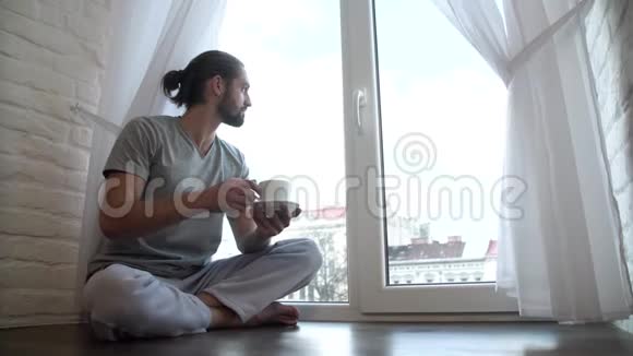 穿睡衣的男人喝咖啡坐在窗户上视频的预览图