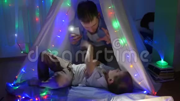 家庭乐趣父亲在儿童帐篷里挠痒痒蹒跚学步夜晚灯火辉煌视频的预览图