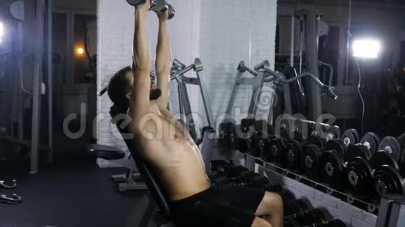 男性运动坐姿训练手臂肌肉使用哑铃在健身房举起手看镜子视频的预览图