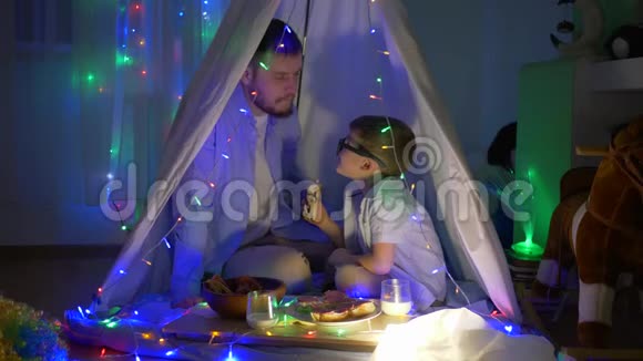 男人的秘密小男孩和爸爸一边闲聊一边坐在帐篷里孩子们的房间里灯火通明视频的预览图