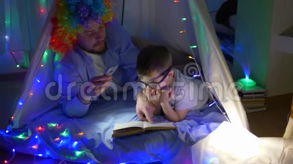 快乐的小丑和孩子一起读杂志然后在带花环的神奇帐篷里睡觉视频的预览图