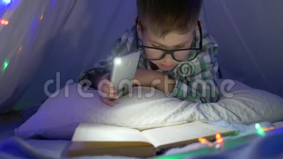 戴眼镜的孩子看书手拿手电筒拿手机视频的预览图