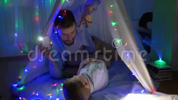 快乐的童年长胡子的父亲和孩子们一起在帐篷里玩晚上在假期里有明亮的灯光视频的预览图