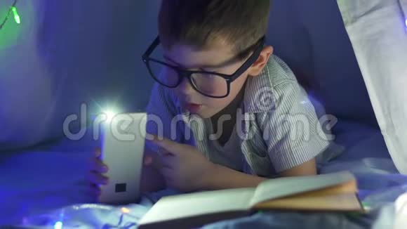 家庭教育快乐的男孩戴着手电筒在帐篷里看童话视频的预览图