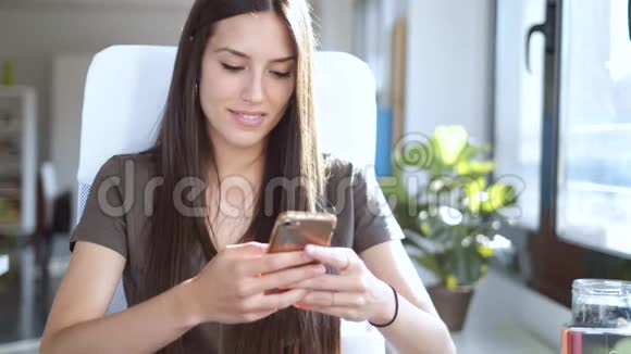 微笑着年轻的商务女性坐在办公室里用手机发送信息视频的预览图