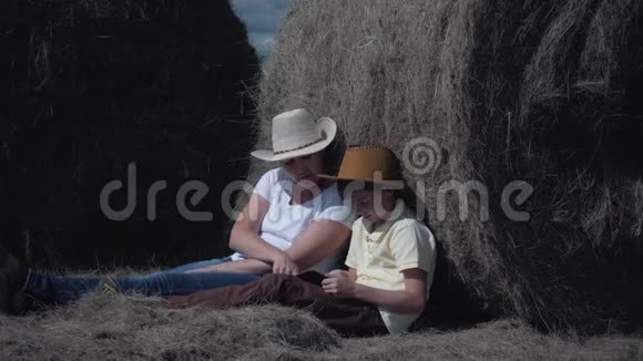 幸福的家庭母子带着平板电脑坐在田里靠在干草卷上幸福家庭的概念视频的预览图