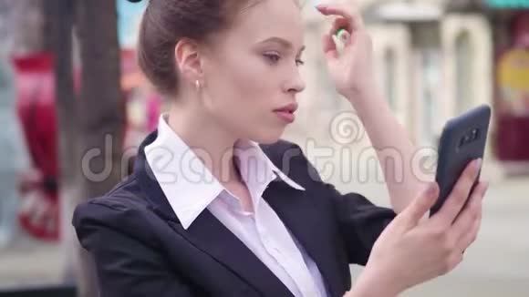 街上的商务女士用一台面向前方的智能手机相机作为镜子来描绘嘴唇视频的预览图