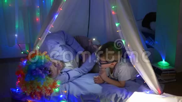 家庭休闲快乐的孩子爸爸戴着小丑假发讲着帐篷里的可怕故事视频的预览图