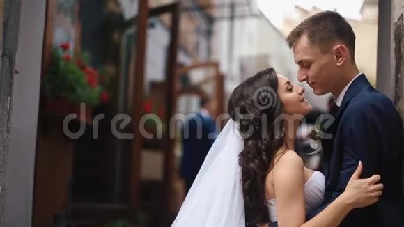 侧面拍摄的年轻迷人的新婚夫妇轻轻地亲吻而倚在墙上的街道视频的预览图