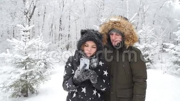 冬季旅行概念快乐的年轻夫妇在户外的智能手机上自拍背景是雪林视频的预览图