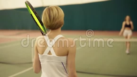 两名参加比赛的女网球运动员欢呼雀跃地互相问候在覆盖的网球场地区握手视频的预览图