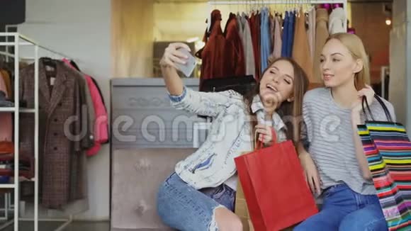 有魅力的女性朋友用智能手机自拍坐在五颜六色的纸袋的服装店里视频的预览图