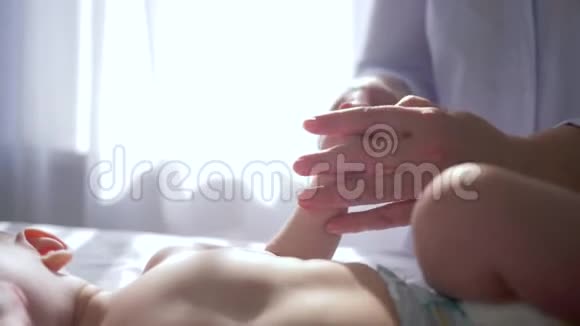 在明亮的窗户特写背景下治疗师将新生儿的手捏在桌子上视频的预览图