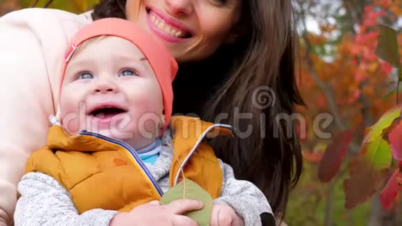 秋天城市公园黄树背景下妈妈在宝宝身边用口水特写的幸福家庭肖像视频的预览图