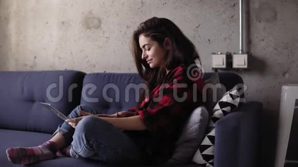 20的漂亮女孩正在沙发上发冷她正在用手提电脑键盘打字视频的预览图