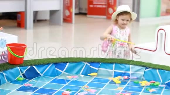 操场上的小女孩玩一个钓鱼游戏在游泳池里钓到鱼然后把它堆在桶里视频的预览图