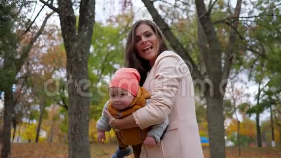 妈妈和孩子一起在秋天的公园玩耍一家人在背景树上玩得很开心视频的预览图