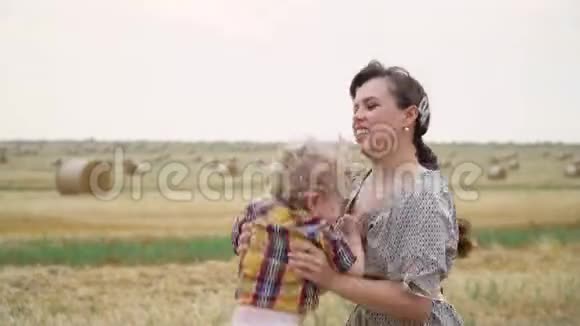 一个年轻的女人一个金发的小儿子抱在她的怀里在一个麦田里夏天的晚上带着包视频的预览图