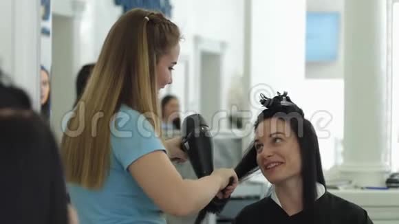 时尚造型师理发店里女孩在理发时借助吹风机与理发师交谈视频的预览图