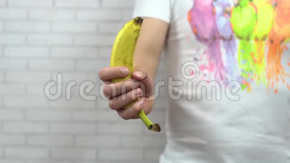 一个穿着白色T恤的年轻人在浅色背景下将成熟的黄色香蕉剥成两半视频的预览图