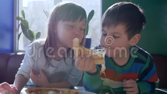 孩子们的食物小男孩和女朋友在靠近窗户的食堂吃奶酪披萨视频的预览图