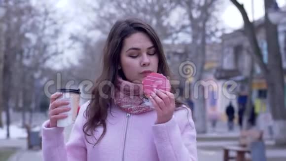 街上的食物年轻的女人吃美味的糕点喝塑料杯咖啡视频的预览图