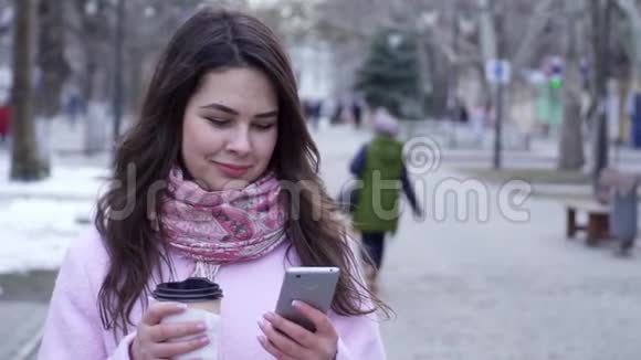 咖啡时间到了女士正坐在互联网上手拿塑料杯的智能手机在街上特写视频的预览图