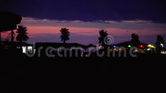傍晚的棕榈树景观沿着傍晚舒适的咖啡馆和日落后的紫色云彩的道路视频的预览图