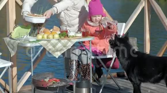 母亲和女儿一个年轻的女人和一个穿暖和衣服的小女孩打开一个罐子一只狗在附近玩耍在旁边野餐视频的预览图
